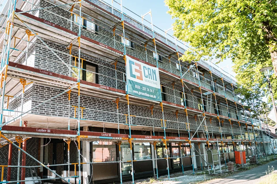Mehrgeschossiges Fassadengerüst mit CAN-Banner und Bäumen am Straßenrand