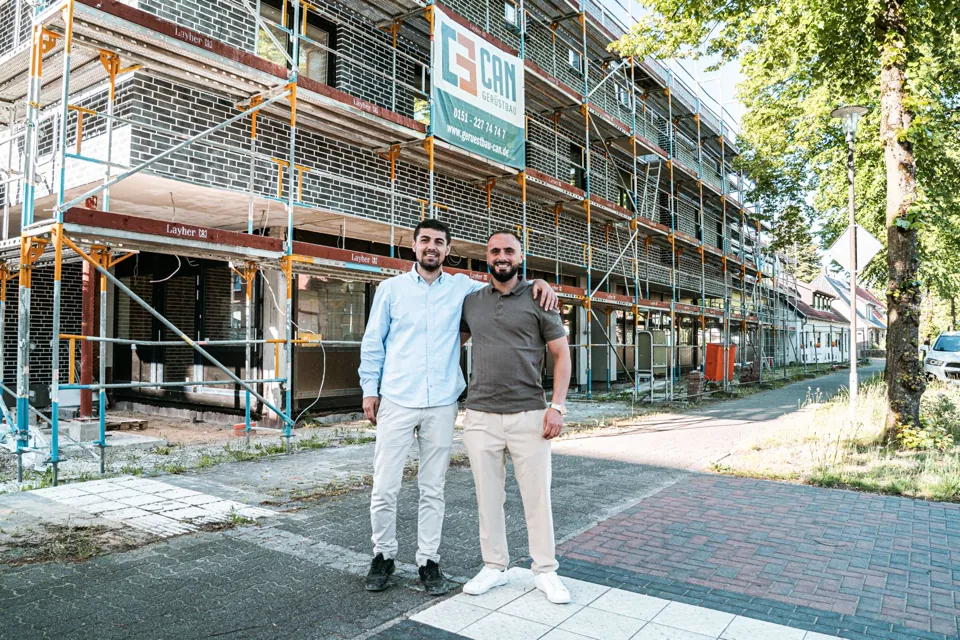 Zwei Personen vor einem eingerüsteten Gebäude mit CAN-Banner