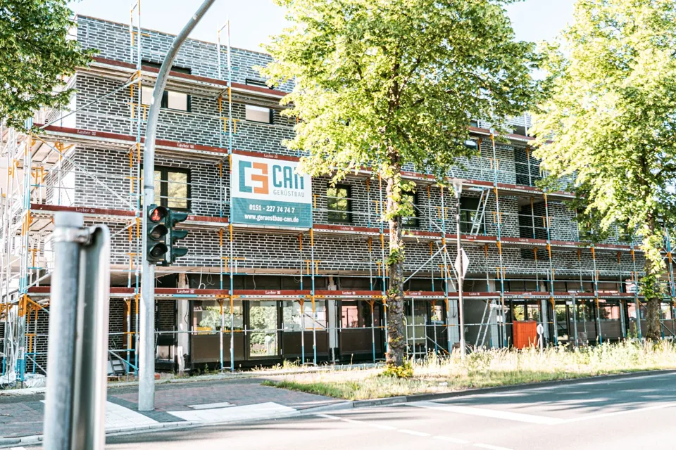 Eingerüstetes Gebäude an einer Straße mit Bäumen und Ampel