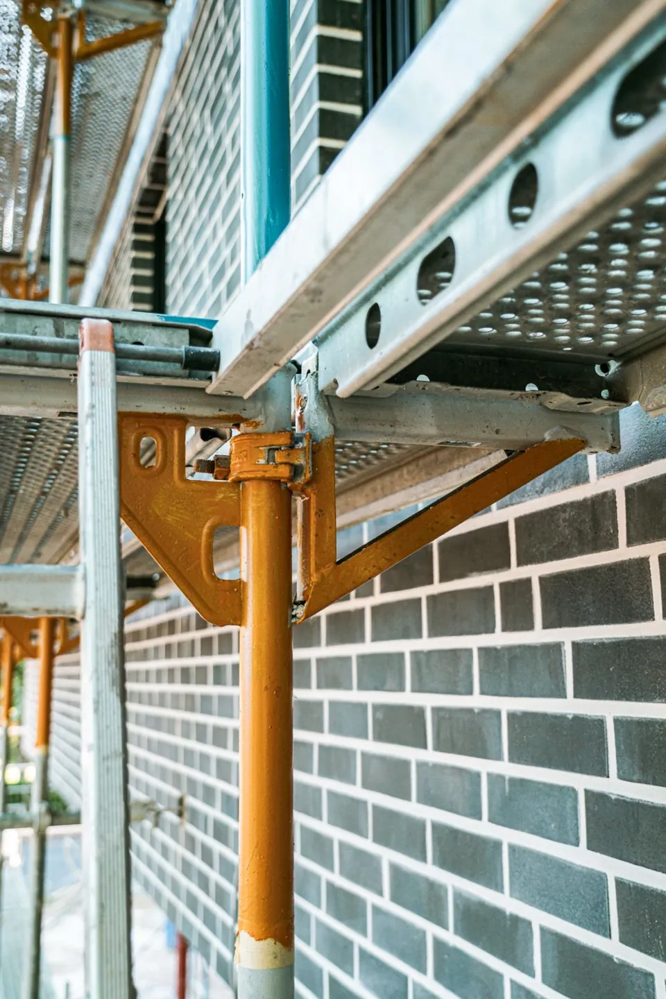 Detail von Gerüststützen und Belägen vor einer dunklen Klinkerfassade